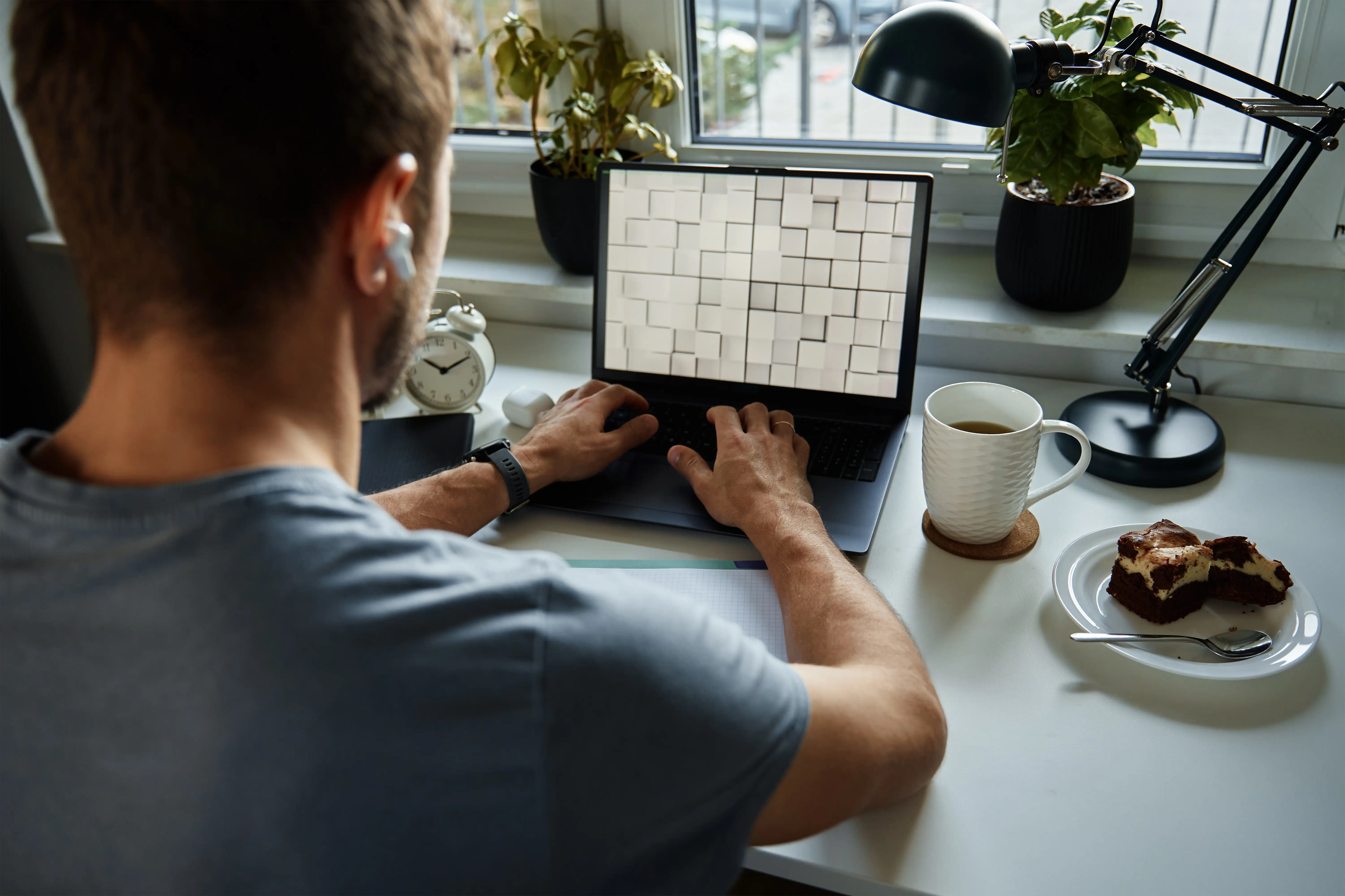 Freelancer im Homeoffice: Ein Mann sitzt am Tisch, arbeitet am Laptop und schreibt in ein Notizbuch.